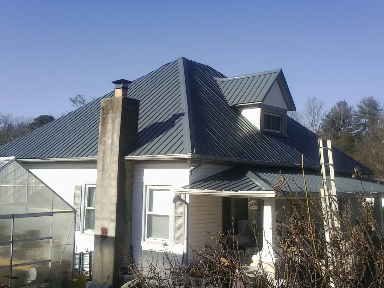 Dark blue standing seam metal roof on a white farmhouse with dormer — Slate & Tile Roof Repair by Roofing Brothers in Marine