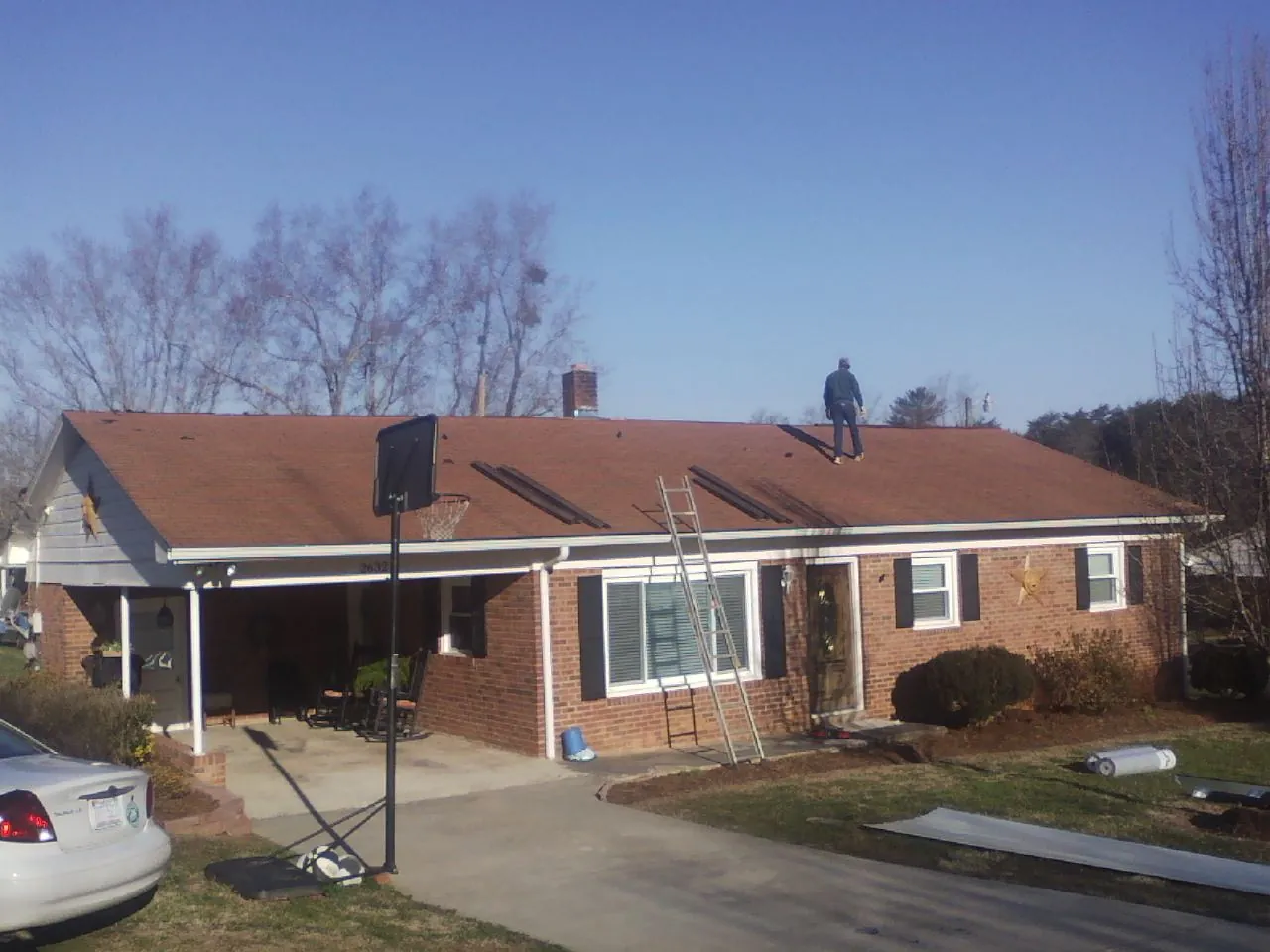 Roofer stripping a shingle roof on a brick ranch before metal panels in Marine