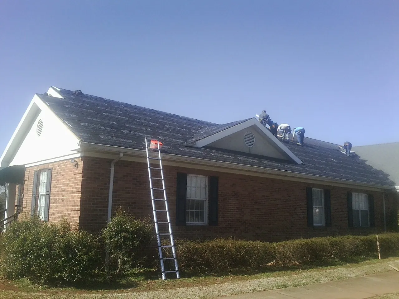 Crew tearing shingles off a brick ranch roof with a ladder set — Emergency Roof Repair work by our crew in Marine