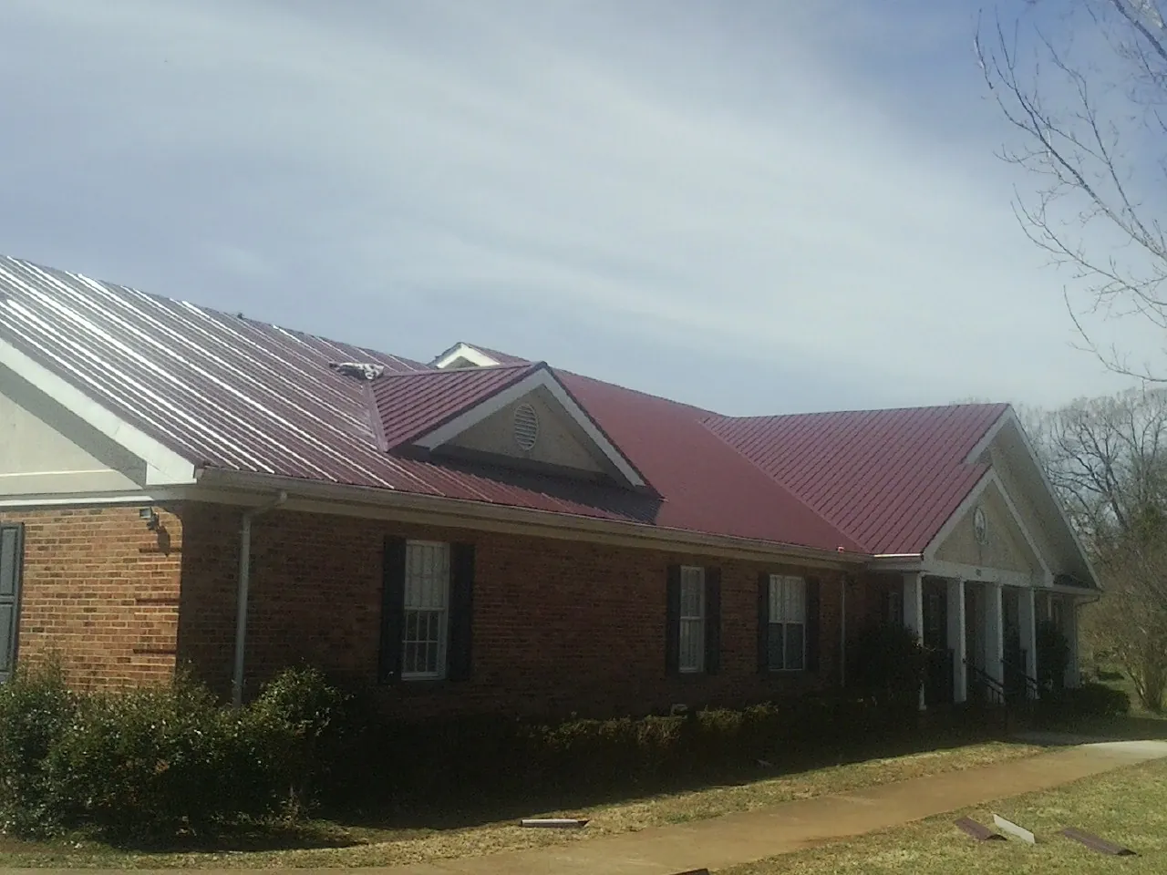 Red metal roof with gabled entries on a long brick building, from a Hail Damage Roof Repair job in Marine