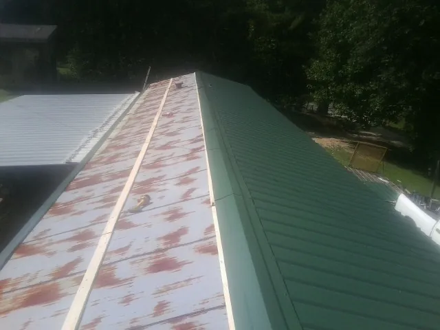 Old rusted panels beside newly installed green metal roofing — Wind Damage Roof Repair by Roofing Brothers in Marine