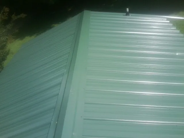 New green metal panels meeting at the ridge of a roof — Flat Roof Repair work by our crew in Marine