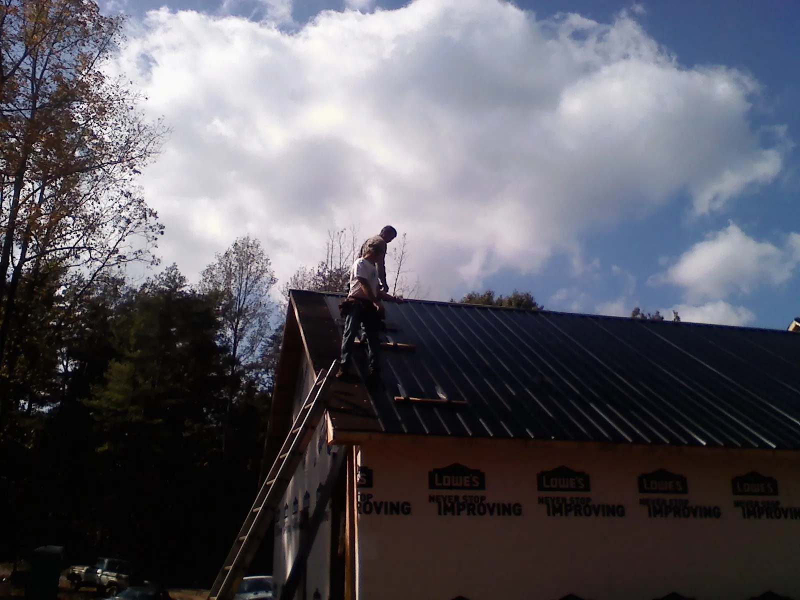 Roofer fastening dark metal panels high against a cloudy sky, from a Roof Inspection job in Marine