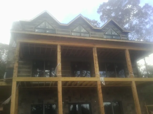 Dormers and porch framing on a large log home under construction — Roof Coating work by our crew in Marine