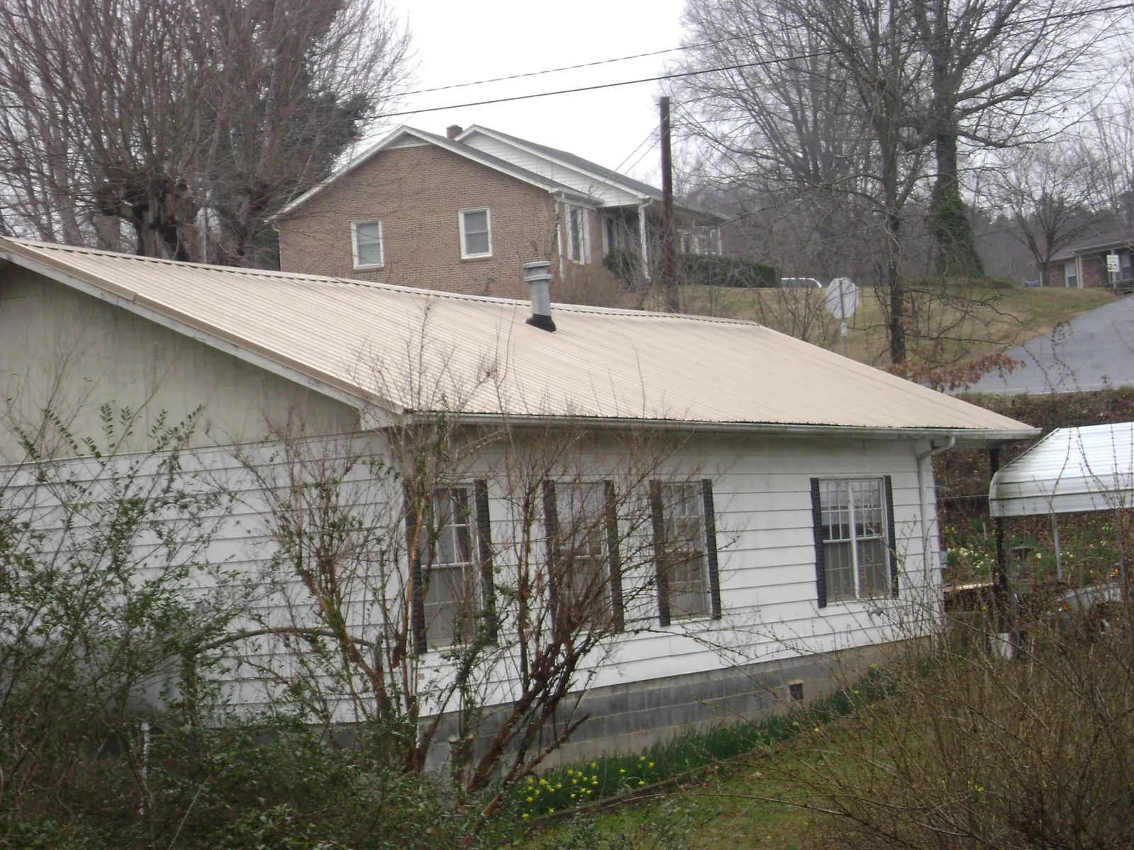 Tan metal roof on a white sided house set into a hillside — Commercial Roofing by Roofing Brothers in Marine